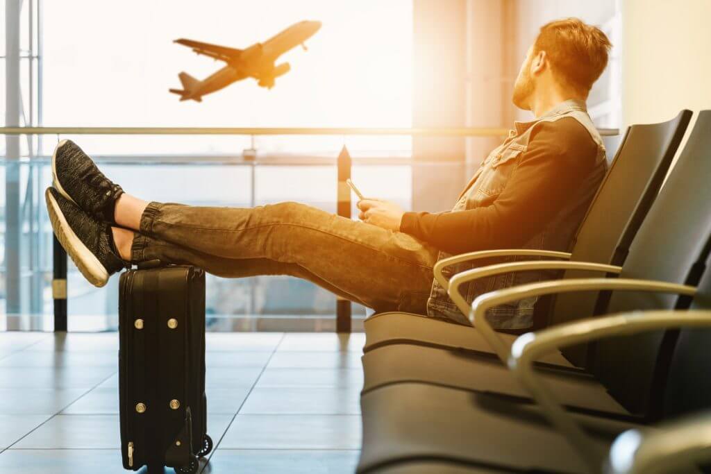 Man Sitting Airport Waiting with Phone feet crossed on luggage bag